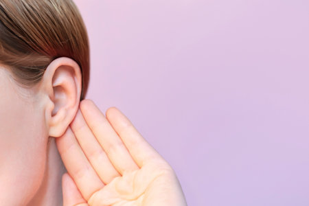 The girl listens attentively with her palm to her ear close-up, the news concept.の写真素材