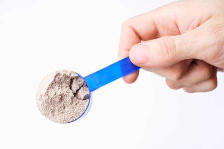 Male hand holding measuring spoon with brown protein top view.の写真素材