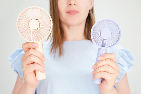 Young woman holding two mini fans on a white background close-up.の写真素材