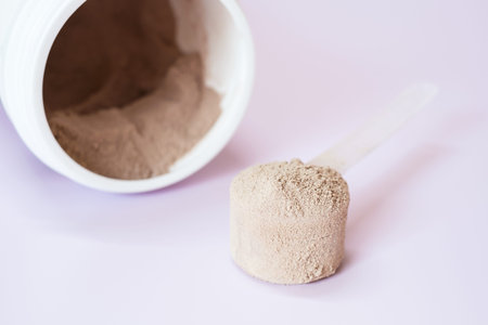Brown protein powder in scoop and plastic jar on lilac background.の写真素材