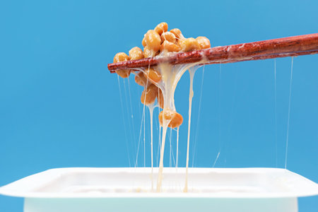 Japanese fermented natto beans on wooden chopsticks on a blue background.