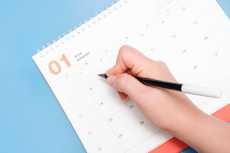 Calendar for January 2024 and female hand on a blue background, planning concept.の写真素材