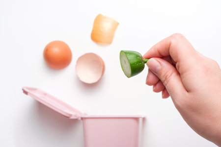 Female hand throwing out food waste leftover into a plastic pink trash can on a white background,...