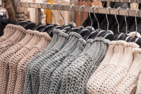 Multicolored knitted sweaters hanging on hangers in a clothing store close up.の写真素材