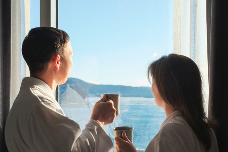 Young man and woman looking out window and holding mugs of coffee, concept of travel or family relationships.の写真素材