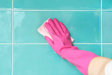 Female hand in pink gloves wipes mint tiles in the bathroom, front view.