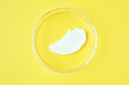 Smear of moisturizing cream in Petri dishes on yellow background close up.の写真素材