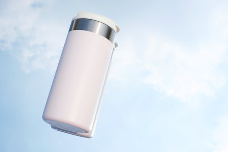 White thermos against the background of a blue sky with clouds close-up.の写真素材