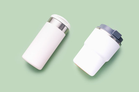Two white thermo mugs on a green background top view close up.