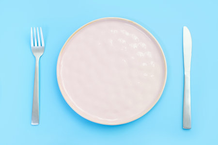 Empty plate on blue background, intermittent fasting concept.の写真素材