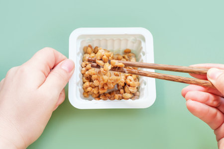 Female hand holding chopsticks with natto beans on green background, top view.の写真素材