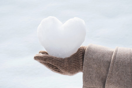 Female hand in brown glove holding heart shaped snowball on white background.の写真素材