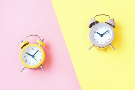 Two small alarm clocks on pink and yellow background close up top view.の写真素材