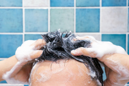 Male hands wash their hair with shampoo and foam against background of blue tiles, front view.の写真素材
