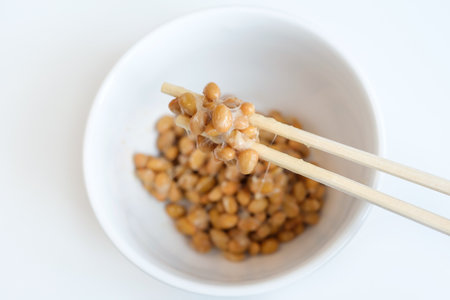 Wooden chopsticks holding japanese natto beans on white background top view.の写真素材