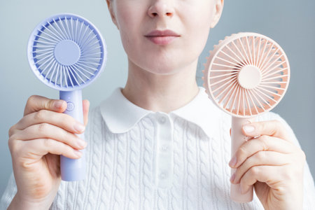 Young woman holding two mini fans on a gray background close-up, front view.の写真素材