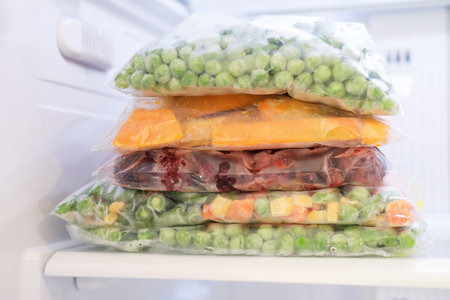 Cellophane bags with colorful frozen vegetables in freezer front view.の写真素材