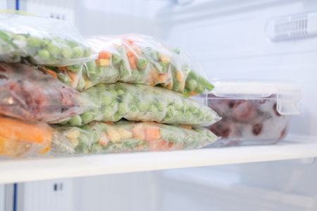 Bags with frozen vegetables and glass box with cherries on the shelf in the refrigerator.の写真素材