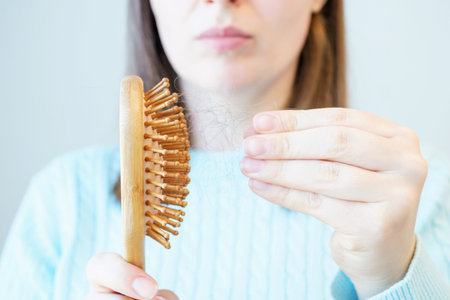Portrait of a young woman taking out fallen hair from a wooden comb front view close-up on a gray...