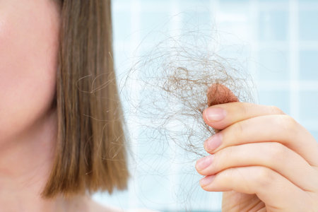 Woman holds a strand of hair against background of blue tiles, hair loss concept.の写真素材