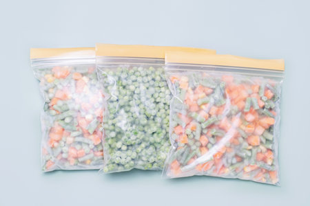 Three zip bags with frozen sliced vegetables on green background close-up top view.の写真素材