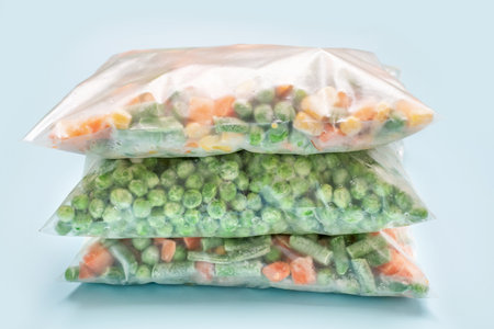 Stack of bags with frozen vegetables on blue background close-up.の写真素材