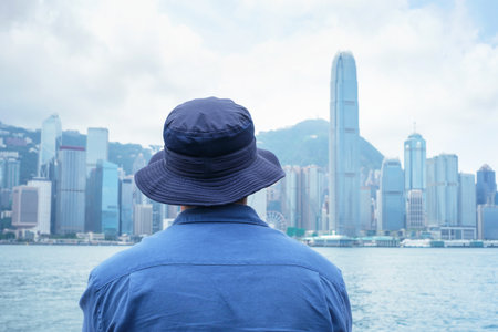 Man in blue shirt standing on embankment and looking at beautiful views of skyscrapers in the Hong Kong rear view.の写真素材