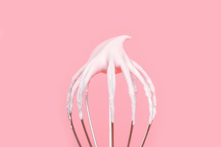 Whisk with whipped cream from proteins close up on pink background.の写真素材