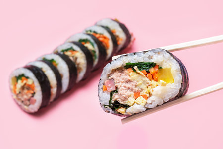 Wooden chopsticks with Korean kimbap roll on pink background close up.の写真素材