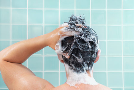 Male hands wash their hair with shampoo and foam against background of mint tiles, rear view.の写真素材