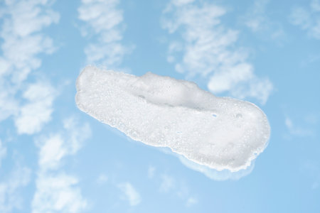 Smear of facial cleansing foam against background of a blue sky and clouds.の写真素材