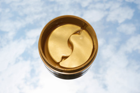 Jar with gold moisturizing eye patches on blue sky background with clouds close up top view.の写真素材
