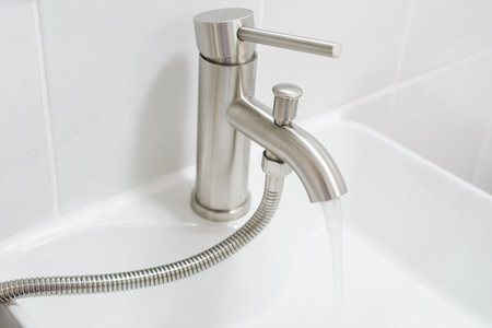 Water flows from a tap into a sink on a gray background close up.の写真素材