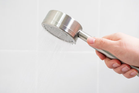 Female hand holding white shower head on white tile background close up, side view.の写真素材