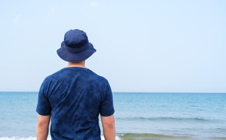 Man in blue t-shirt and panama hat standing on a seashore back view concept of rest and travel.の写真素材