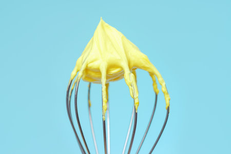 Whisk with yellow whipped cream from proteins close up on blue background.の写真素材