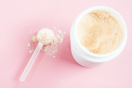 Protein powder in scoop against plastic jar on a pink background, top view.の写真素材
