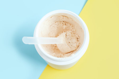 Protein powder in scoop and plastic jar on a blue and yellow background.の写真素材