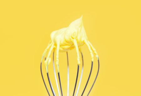 Whisk with yellow whipped cream from proteins close up on yellow background.の写真素材