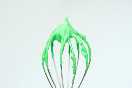 Whisk with green whipped cream from proteins close-up on gray background.
