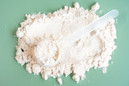 Scoop lies on scattered protein powder close-up view from above on green background.の写真素材