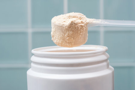 Protein powder in scoop and plastic jar on blue tile background close-up.