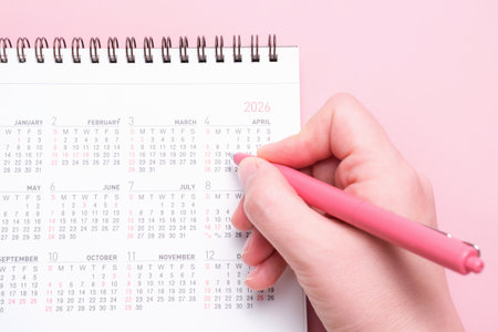 Calendar and female hand with pen on pink background close-up top view.の写真素材