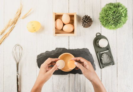 Top view of woman chef breaking an egg into the wood bowl. Cooking concept.の写真素材