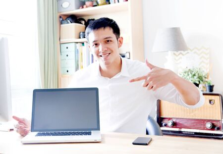 A Portrait of young asian man working with laptop  and showing gesture signの写真素材