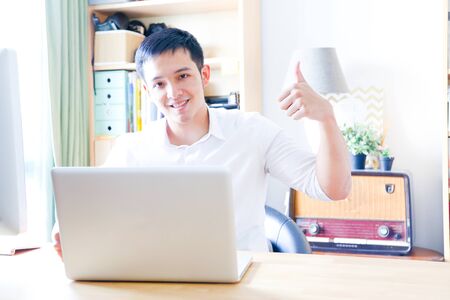 A Portrait of young asian man working with laptop  and showing gesture signの写真素材
