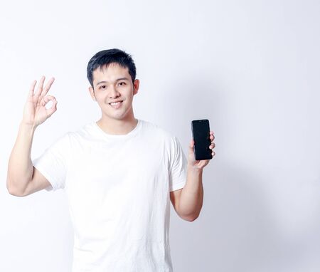 A Portrait of young asian man in white shirt and blue jeans  showing gesture sign or devicesの写真素材
