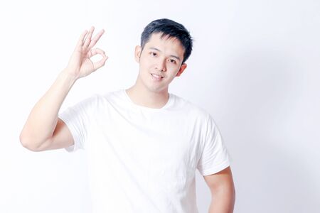 A Portrait of young asian man in white shirt and blue jeans  showing gesture sign or devicesの写真素材