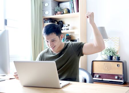 young asian wearing a green tshirt working with laptop in home officeの写真素材