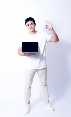 A Portrait of young asian wearing a Green t-shirt and white jeans showing gesture sign or devicesの写真素材